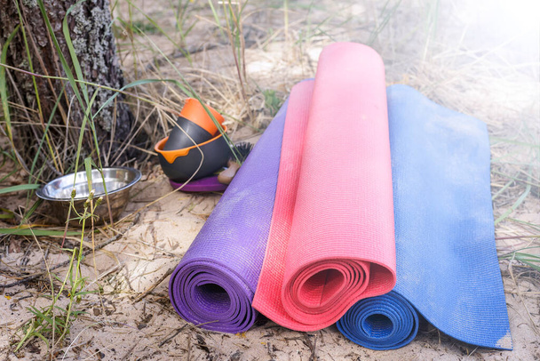 Três tapetes de ioga na praia arenosa da floresta, situado perto dos utensílios de cozinha acampamento (copos, pratos) e um pente
. - Foto, Imagem
