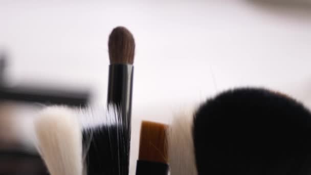 Many makeup brushes on blurred background, closeup - Séquence, vidéo