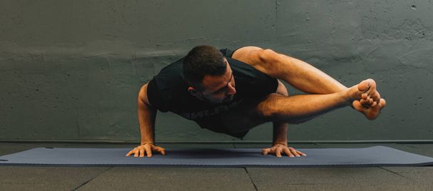 Sportif genç adam amuda kalkma yogası yapıyor. Fotokopi alanı için gri arkaplan ile kentsel fitness salonunda stüdyo çekimi. - Fotoğraf, Görsel