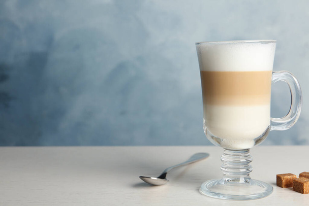 Delicious latte macchiato and sugar cubes on white table against light blue background, space for text - 写真・画像