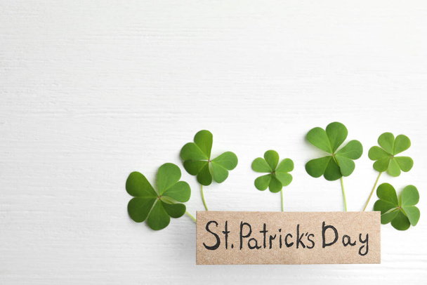 Clover leaves and card with text ST. PATRICK'S DAY on white wooden table, flat lay. Space for text - Foto, Imagem