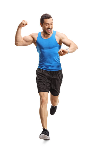 Full length portrait of a male athlete running towards the camera and checking time on smartwatch isolated on white background - Φωτογραφία, εικόνα