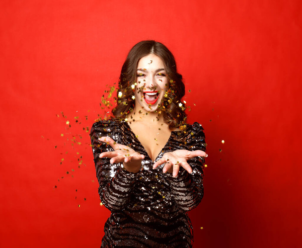 beautiful girl wearing evening dress standing standing under confetti rain over red background - Photo, image