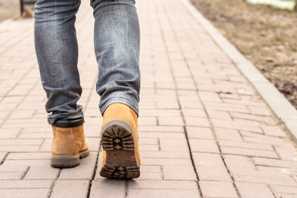 As pernas de um homem de botas amarelas em uma estrada de pedra pavimentada em um dia ensolarado de primavera. Close-up
. - Foto, Imagem