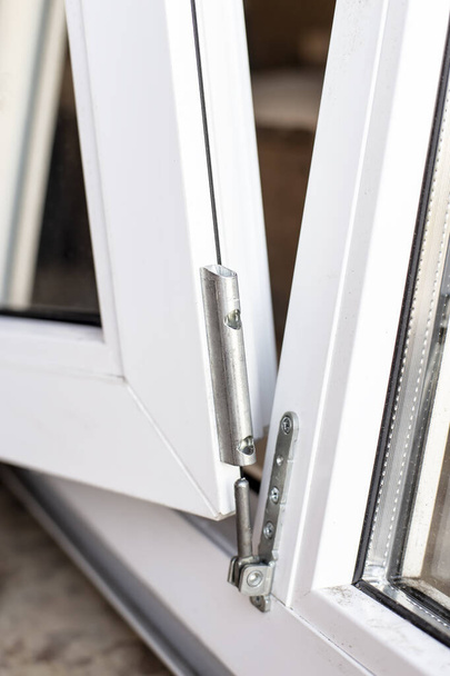Der bewegliche Teil des PVC-Fensters wird mit einem Metallscharnier mit dem Rahmen verbunden. Nahaufnahme. - Foto, Bild