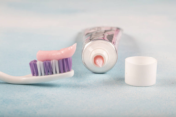 Spazzolino con dentifricio rosa accanto a un tubo di dentifricio sullo sfondo blu
  - Foto, immagini
