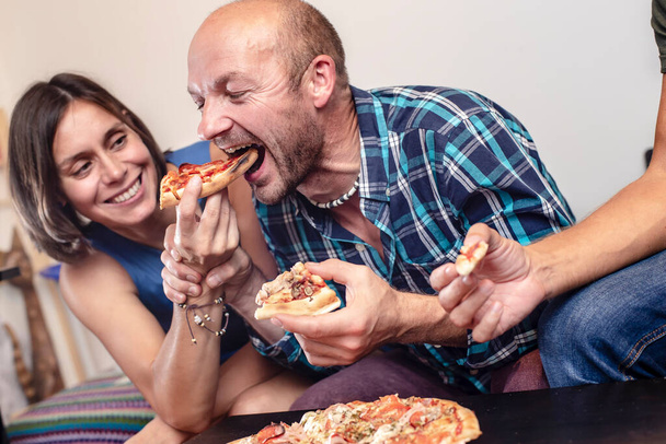 Soirée maison. Des amis mangeant et s'amusant. Homme prend ludique une tranche de pizza de la femme souriante. - Photo, image