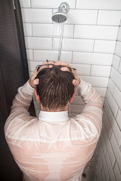 Müder Geschäftsmann im weißen Hemd, die Hände hinter dem Kopf, den Rücken in der Dusche unter fließendem warmen Wasser nach einem harten Arbeitstag. - Foto, Bild