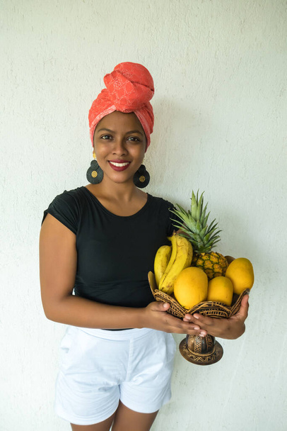 Een Afro-Amerikaanse vrouw met een mand van ananas, banaan en mango. - Foto, afbeelding