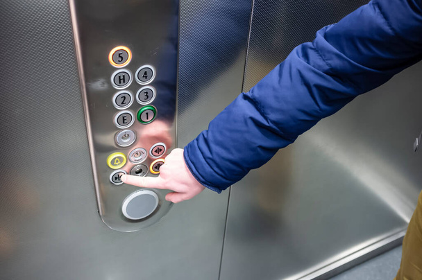 Egy férfi kék kabátban a liftben megnyomja az ujját a gombon, hogy becsukja az ajtót. - Fotó, kép