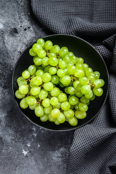 A branch of green juicy grapes in a plate. Black background. Top view. - Foto, Bild