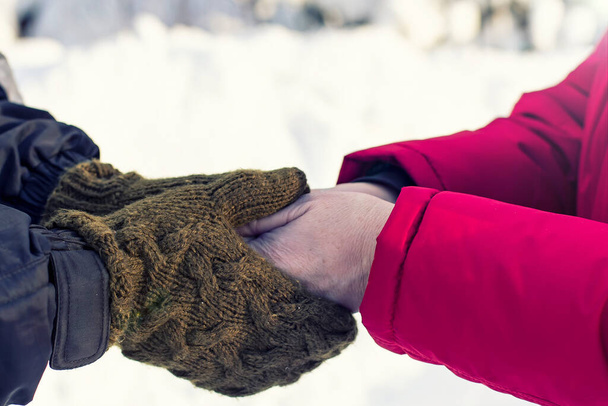 Les mains de son fils dans des mitaines en laine chaude tiennent et réchauffent les mains de la mère qui n'a pas de gants. Soin et tendresse lors d'une journée hivernale givrée. - Photo, image