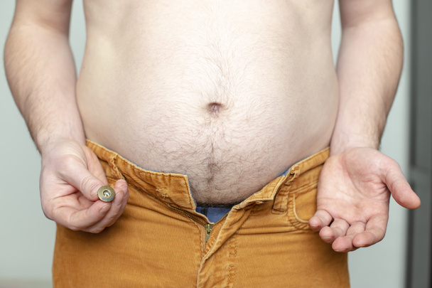 Tlustý člověk utrhl knoflík, snažil se zapnout staré kalhoty, byl překvapen a přemýšlel o tom jít do fitness klubu - Fotografie, Obrázek