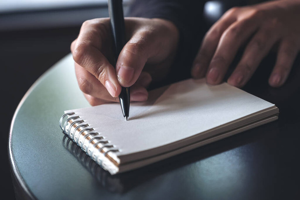 Imagen de cerca de las manos de una mujer anotando en un cuaderno blanco en blanco en la mesa  - Foto, imagen