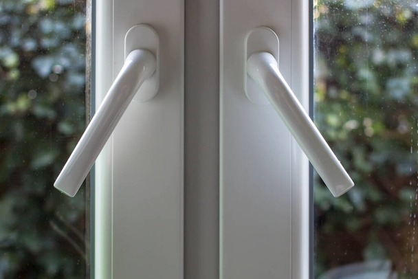 Handles on PVC structures are at an angle and the windows are not completely closed, with dusty glass through which you can see green bushes in the garden. Close-up. - Photo, Image