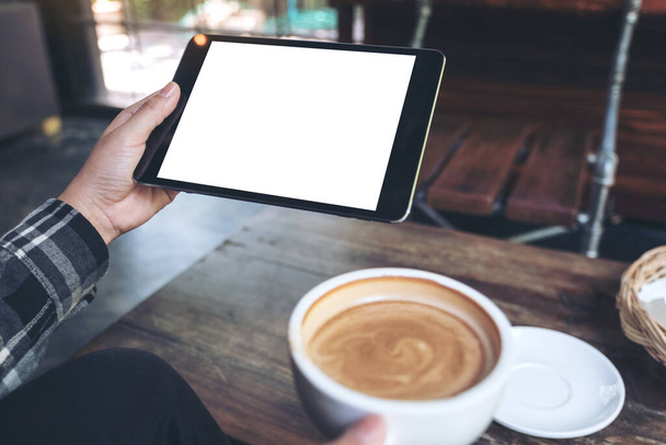 Mock up imagem de mãos segurando tablet preto pc com tela branca em branco enquanto bebe café no café - Foto, Imagem