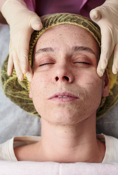 Le cosmétologue nettoie la peau du visage du patient à l'aide d'un gommage au bureau. Gros plan. - Photo, image