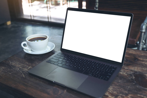 Mockup image of laptop with blank white desktop screen and coffee cup on wooden table in modern cafe - 写真・画像