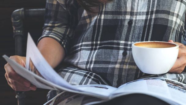 Closeup image of a woman reading a book while drinking coffee in modern cafe  - 写真・画像
