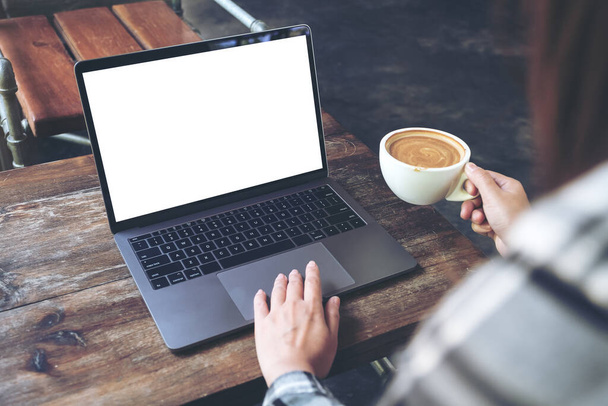 Εικόνα mockup μιας γυναίκας που χρησιμοποιεί laptop με λευκή οθόνη ενώ πίνει ζεστό καφέ στο cafe - Φωτογραφία, εικόνα