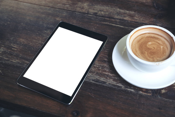Top view makieta obraz czarnej tabletki z białym pustym ekranem pulpitu i filiżanki kawy na zabytkowym drewnianym stole w kawiarni - Zdjęcie, obraz