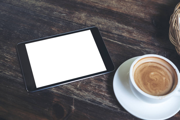 Imagen maqueta vista superior de la tableta negra con pantalla blanca en blanco de escritorio y taza de café en la mesa de madera vintage en la cafetería
 - Foto, Imagen