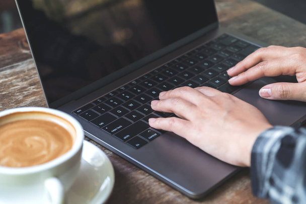 Image rapprochée d'une femme travaillant et tapant sur un clavier d'ordinateur portable avec une tasse de café sur la table
 - Photo, image