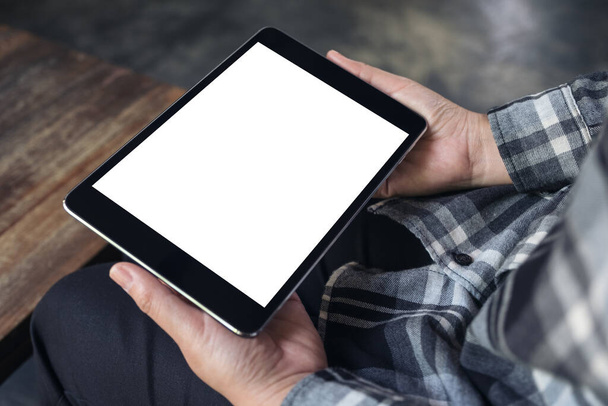 Wizerunek dłoni trzymających czarną tabletkę z białym, czystym ekranem i filiżanką kawy na tle stołu - Zdjęcie, obraz