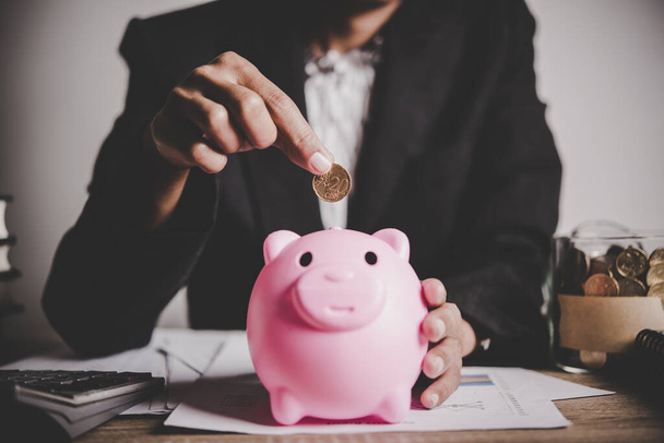 putting  coin into a piggy bank on the table. Financial savings concept - Fotó, kép