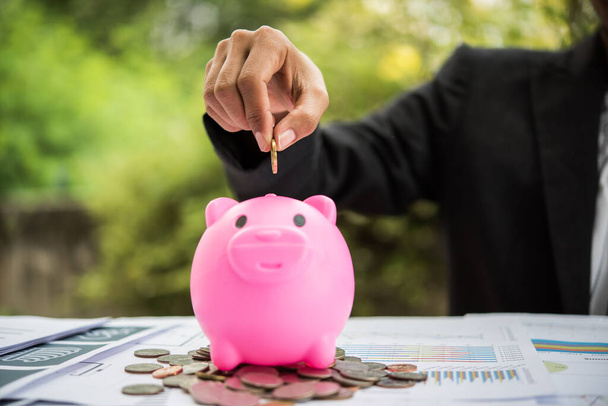 putting  coin into a piggy bank on the table. Financial savings concept - Fotoğraf, Görsel