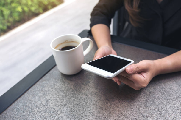 Image rapprochée d'une femme utilisant et regardant le téléphone intelligent avec tasse de café dans le café - Photo, image