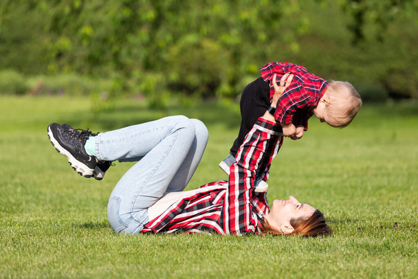 Cute cheerful   baby  with mother hug outdoors in park. Happiness and harmony of family life. Great family vacation. Mother and son have activities together on holidays. - Фото, зображення