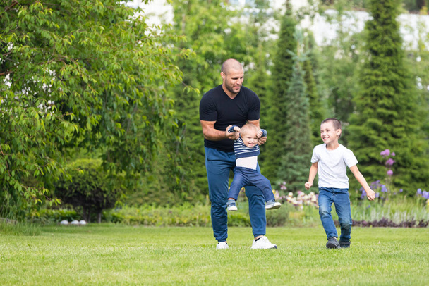Χαριτωμένο χαρούμενο δύο αγόρια αδελφός παιδί με τον πατέρα παίζουν σε εξωτερικούς χώρους στο πάρκο. Ευτυχία και αρμονία της οικογενειακής ζωής. Μεγάλες οικογενειακές διακοπές.  - Φωτογραφία, εικόνα