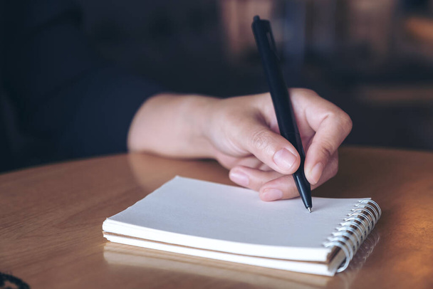 Imagem de close-up de uma mão escrevendo em um caderno em branco na mesa
  - Foto, Imagem
