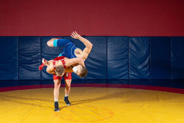 公正なレスリングの概念。ジムで黄色のレスリングカーペットの上で赤と青の均一なレスリングで2人のグレコ-ローマの力士 - 写真・画像