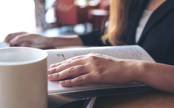 Szoros kép egy üzletasszony olvasás egy könyvet csésze kávé az asztalon kávézóban  - Fotó, kép