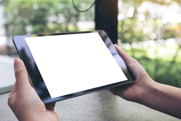 Mockup image of hands holding black tablet pc with blank white desktop screen on the table - Photo, Image