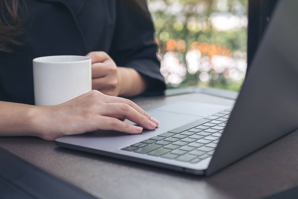 Imagen de primer plano de trabajo a mano y mecanografía en el teclado del ordenador portátil mientras bebe café en la oficina
 - Foto, imagen