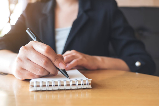 Nahaufnahme einer Geschäftsfrau, die auf ein weißes Blanko-Notizbuch auf dem Tisch im Büro schreibt - Foto, Bild