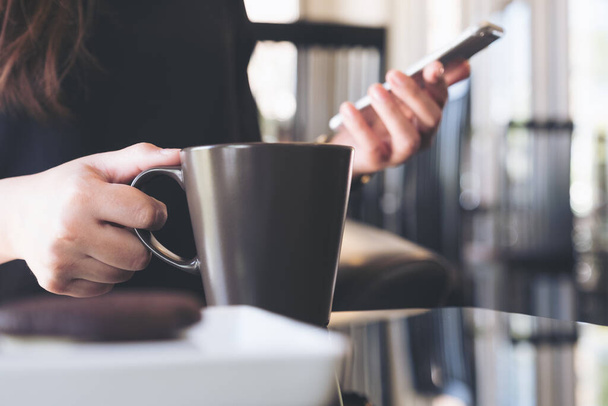 Крупный план женщины, держащей и использующей смартфон во время питья кофе в кафе - Фото, изображение