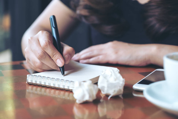 Imagen de cerca de una mujer de negocios trabajando y escribiendo en un cuaderno blanco con papeles jodidos en la mesa
 - Foto, imagen