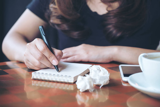 Bir iş kadınının çalışma ve yazı yazma görüntüsü beyaz boş bir defter ve masa üzerinde berbat kağıtlar. - Fotoğraf, Görsel