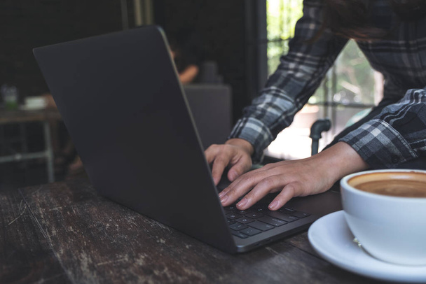Zbliżenie obrazu kobiety pracującej i piszącej na klawiaturze laptopa z filiżanką kawy na stole - Zdjęcie, obraz