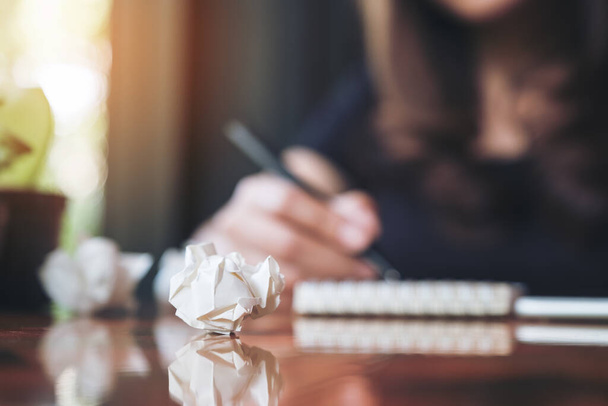 Крупный план деловой женщины, работающей и записывающей на белой пустой блокнот с испорченными бумагами на столе
  - Фото, изображение