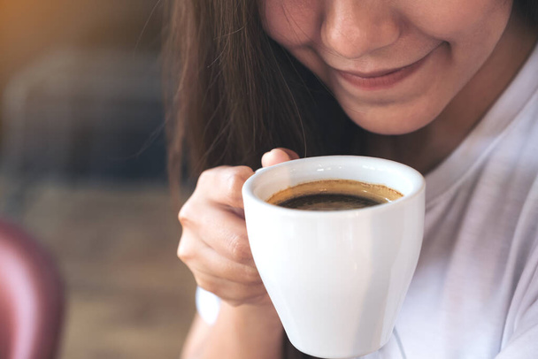 Closeup image of an Asian woman holding a coffee cup before drinking with feeling good in cafe - Foto, Imagem