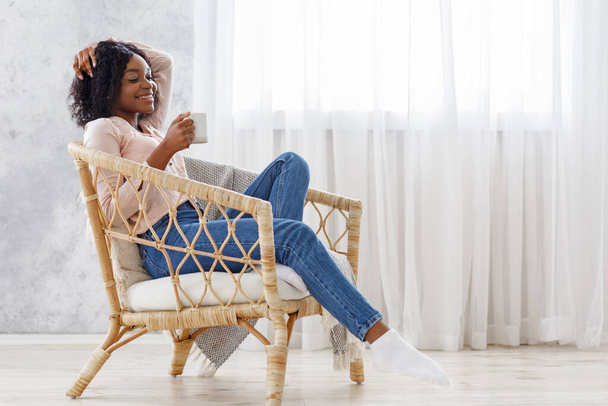E 'ora di rilassarsi. nero donna godendo caffè mentre seduto in moderno sedia
 - Foto, immagini