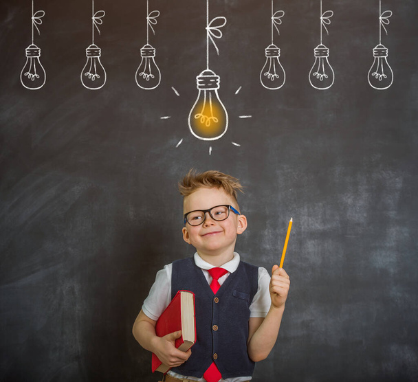 School boy near the blackboard has idea. Kid with drawn bulb pointing up School concept - Фото, зображення
