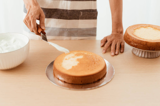 chef van het gebakje zet crème op de taart van een spons. Taart besluitvormingsproces. - Foto, afbeelding
