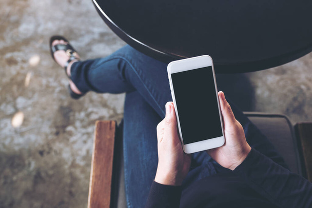 Изображение макета женской руки с белым мобильным телефоном с пустым экраном на бедре в кафе - Фото, изображение