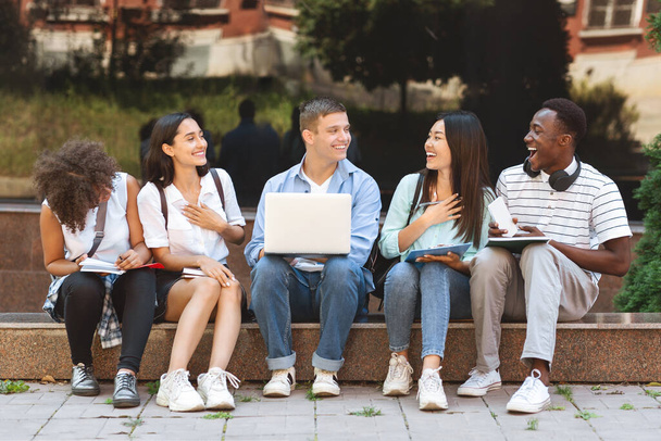 Pause zwischen den Klassen. Glückliche Studenten sitzen auf Bank am Uni-Campus - Foto, Bild